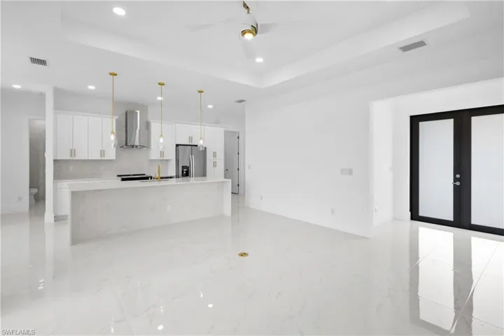 Kitchen with wall chimney exhaust hood, stainless steel fridge, a tray ceiling, and light tile patterned floors