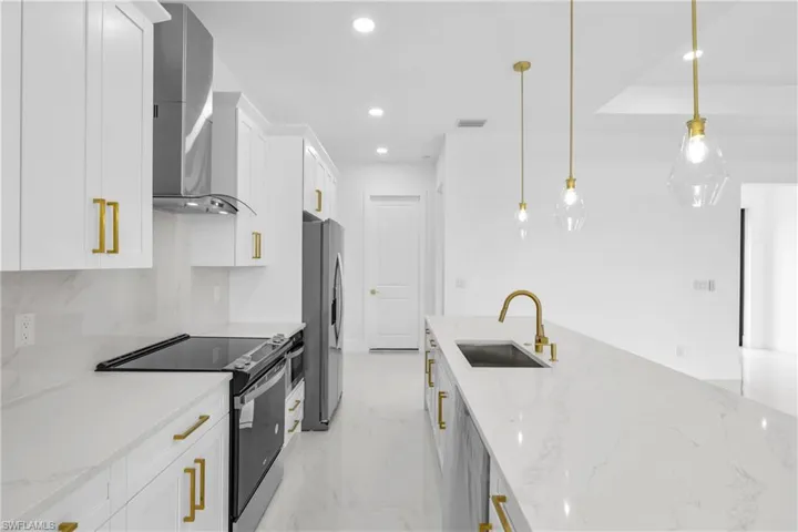 Kitchen with wall chimney exhaust hood, white cabinetry, appliances with stainless steel finishes, sink, and light tile patterned flooring