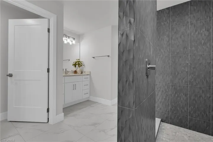 Modern bathroom featuring large format tile flooring, a single vanity with stone countertop, and a shower with textured wall tile