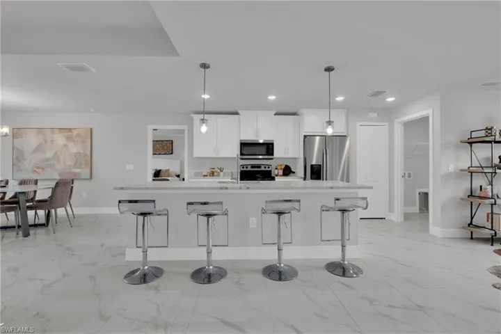 Kitchen island with bar seating, pendant lighting, stainless steel appliances, white cabinetry, and large format tile flooring