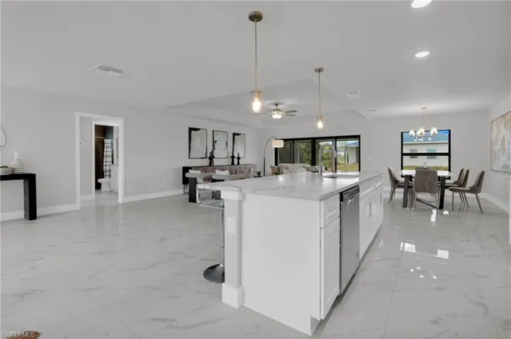 Open-concept living area featuring large format tile flooring, a kitchen island with stone countertop, stainless steel appliances, and a recessed ceiling with modern lighting