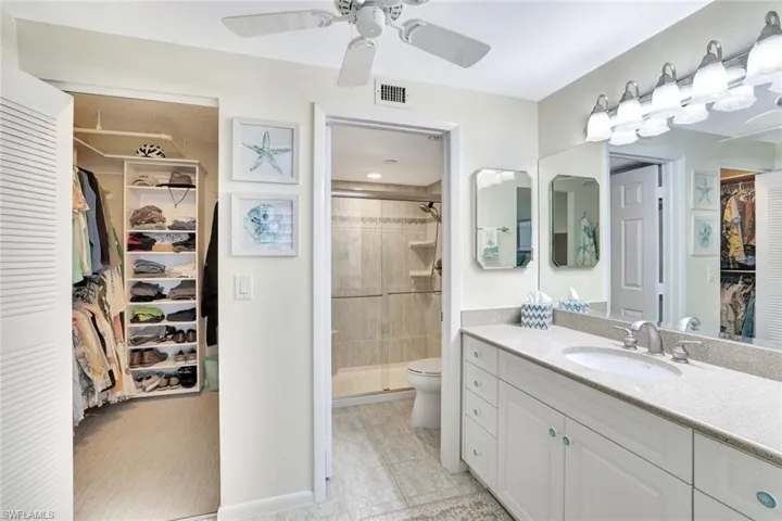 Bathroom featuring a spacious closet, vanity, a stall shower, light tile patterned flooring, and a ceiling fan