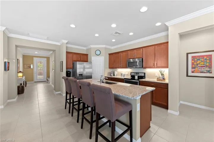Kitchen featuring a breakfast bar, brown cabinetry, stainless steel appliances, crown molding, and an island with sink