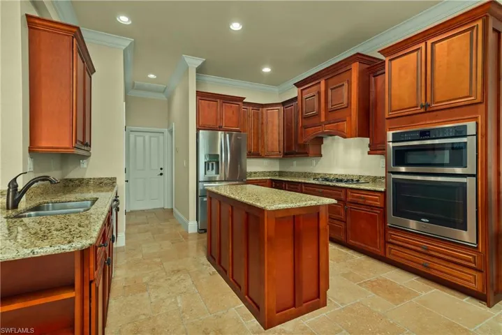 Kitchen featuring stainless steel appliances, a sink, stone tile floors, and light stone countertops