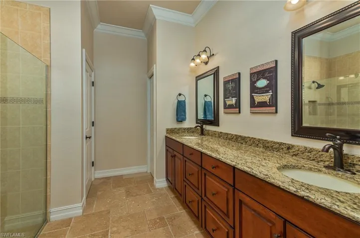 Full bathroom with baseboards, ornamental molding, a tile shower, stone tile flooring, and a sink