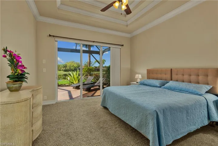 Carpeted bedroom featuring access to exterior, a tray ceiling, a ceiling fan, and ornamental molding