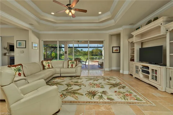 Living room with ceiling fan, baseboards, ornamental molding, a raised ceiling, and stone tile flooring