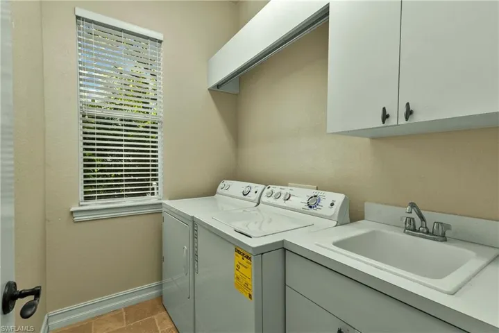 Clothes washing area with cabinet space, baseboards, a sink, and washing machine and clothes dryer