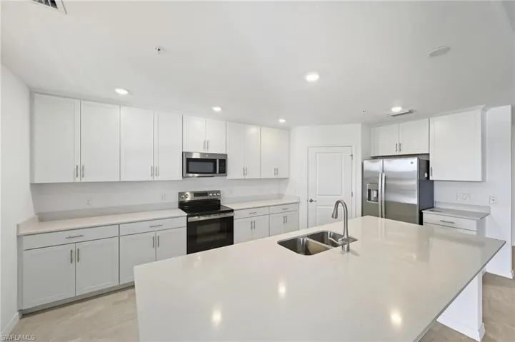Kitchen featuring stainless steel appliances, white cabinetry, an island with sink, recessed lighting, and light stone counters