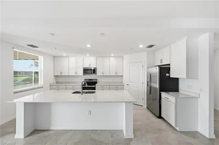 Kitchen featuring white cabinetry, stainless steel appliances, an island with sink, recessed lighting, and light stone counters