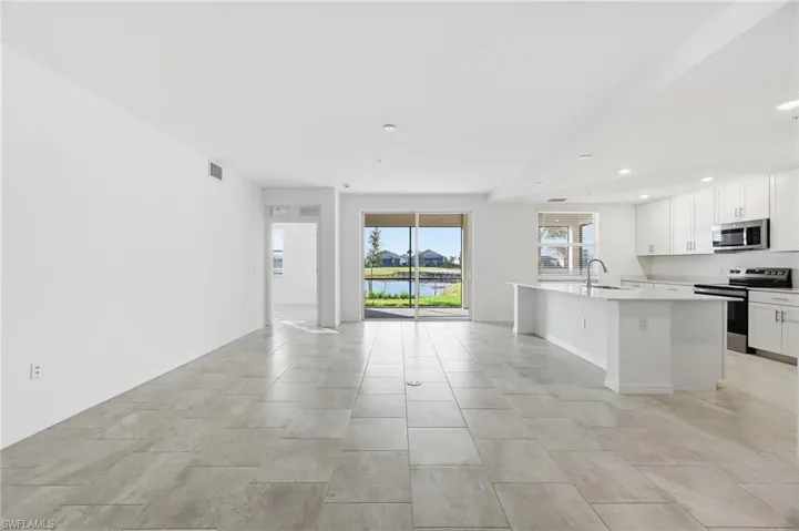 Kitchen with stainless steel appliances, white cabinets, an island with sink, a water view, and open floor plan