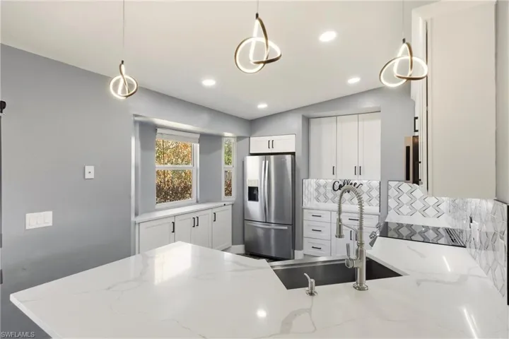 Kitchen featuring hanging light fixtures, white cabinets, tasteful backsplash, stainless steel fridge with ice dispenser, and lofted ceiling