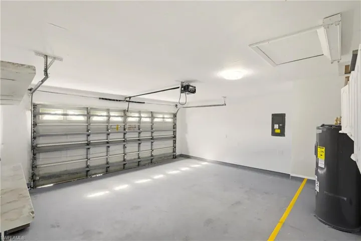 Garage with electric water heater, electric panel, and a garage door opener
