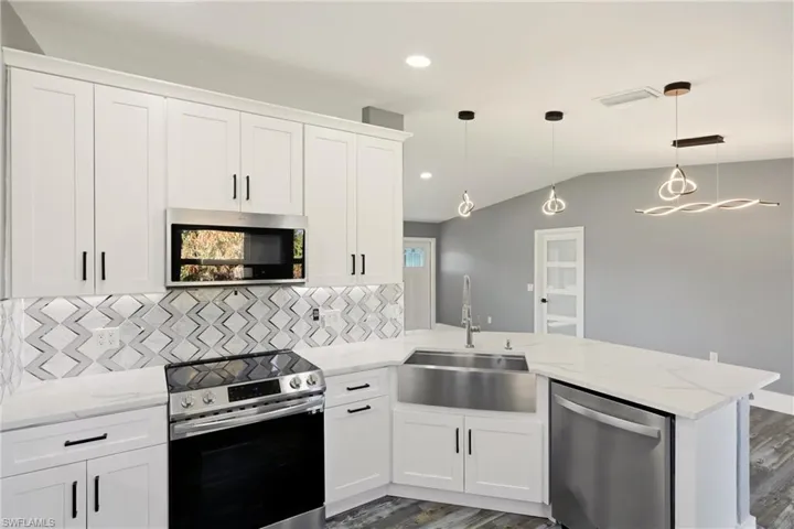 Kitchen featuring stainless steel appliances, white cabinets, decorative light fixtures, a peninsula, and light stone counters