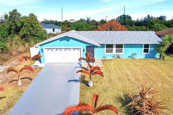 Single story home with stucco siding, driveway, an attached garage, a front lawn, and view of wooded area