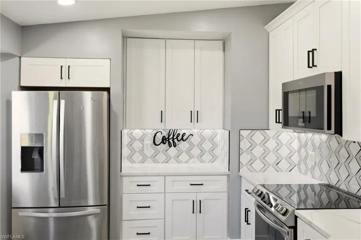Kitchen featuring stainless steel appliances, white cabinetry, light stone countertops, and backsplash