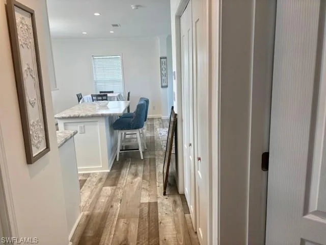 Hall with light wood-type flooring, ornamental molding, and recessed lighting