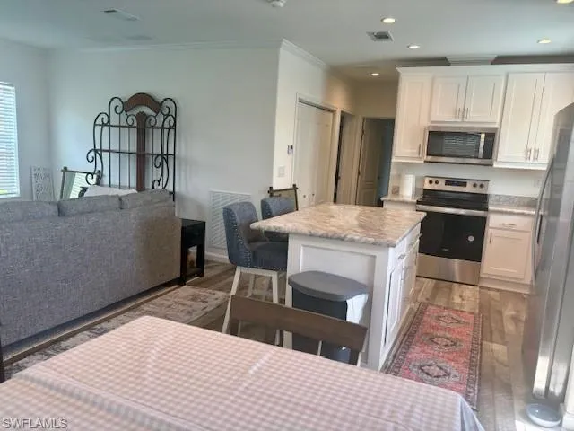 Kitchen with open floor plan, appliances with stainless steel finishes, white cabinetry, a breakfast bar, and crown molding
