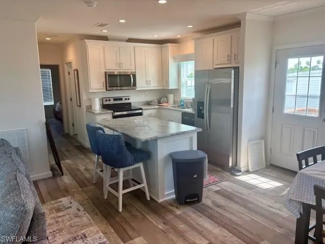 Kitchen with a kitchen bar, appliances with stainless steel finishes, white cabinetry, a center island, and ornamental molding