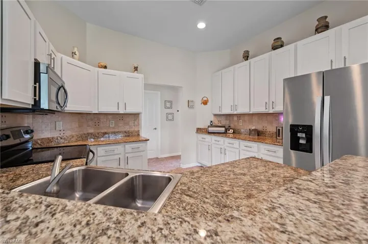 Kitchen featuring decorative backsplash, white cabinets, appliances with stainless steel finishes, and sink