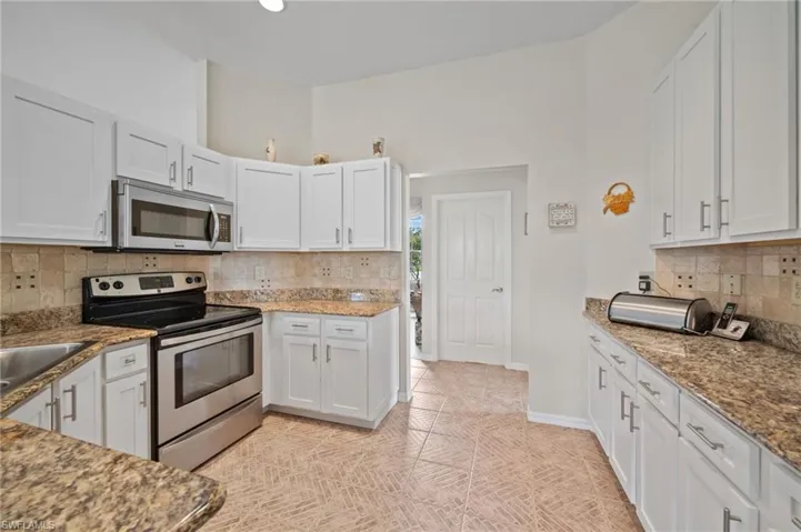 Kitchen featuring tasteful backsplash, stone counters, white cabinetry, appliances with stainless steel finishes, and light tile patterned floors