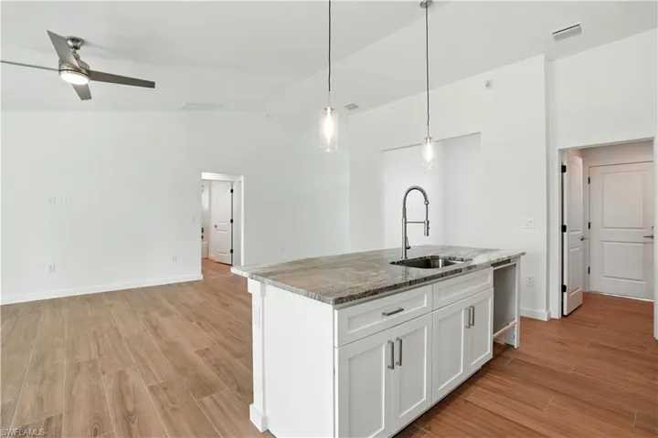 Kitchen with lofted ceiling, light stone countertops, a center island with sink, wood tiled floors, and white cabinets