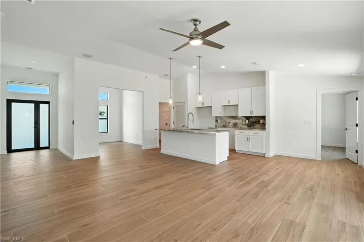 Kitchen with a center island with sink, open floor plan, ceiling fan, white cabinets, and decorative backsplash
