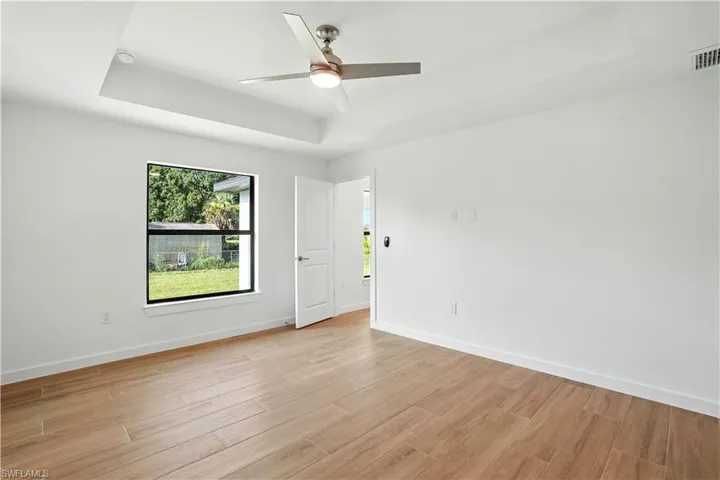 Unfurnished room featuring a raised ceiling, ceiling fan, and light wood-style flooring