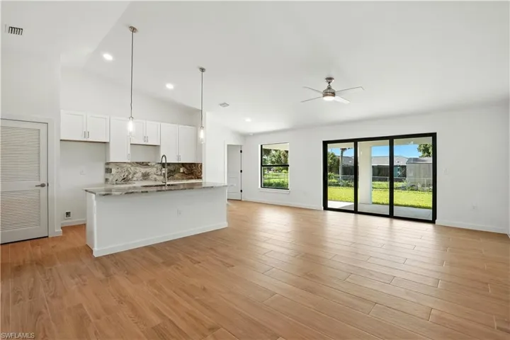Kitchen featuring white cabinetry, tasteful backsplash, a kitchen island with sink, lofted ceiling, and light wood-style flooring