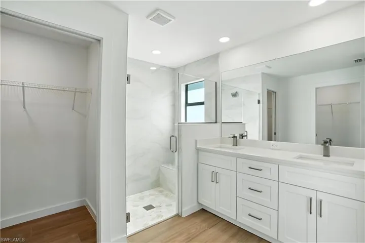 Full bath featuring a walk in closet, light wood-type flooring, a marble finish shower, double vanity, and recessed lighting