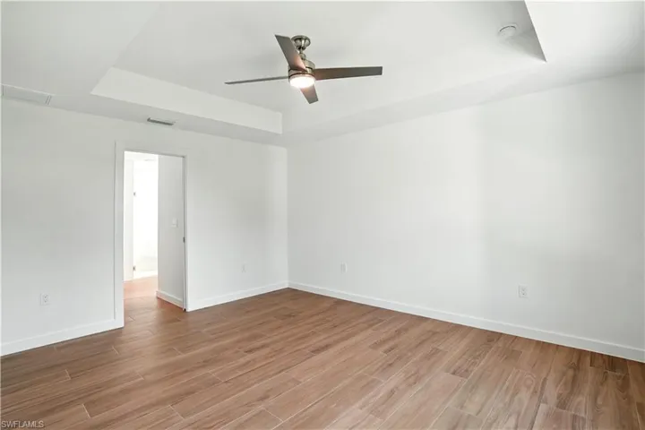 Unfurnished room with a tray ceiling, a ceiling fan, and wood finished floors