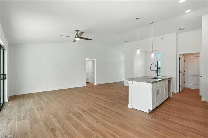 Kitchen featuring open floor plan, wood tiled floors, ceiling fan, an island with sink, and vaulted ceiling