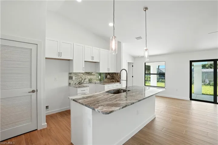 Kitchen with light stone countertops, tasteful backsplash, white cabinetry, light wood finished floors, and vaulted ceiling