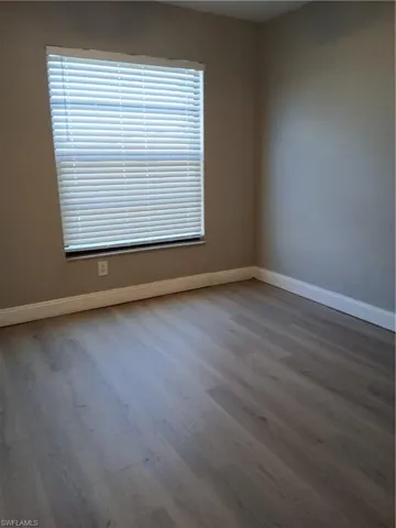 Neutral-toned interior space featuring wood-finish vinyl flooring and a window equipped with horizontal slat blinds. Upstairs guest bedroom