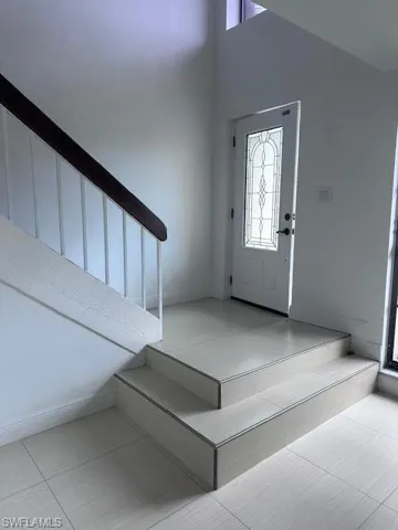 Entryway featuring tile flooring, a tiered staircase with a dark wood handrail, and an exterior door with decorative glass paneling