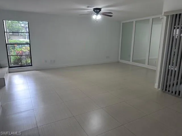 Large-format neutral tile flooring, floor-to-ceiling mirror-paneled walls, a multi-pane fixed window, and an integrated ceiling fan with light fixture
