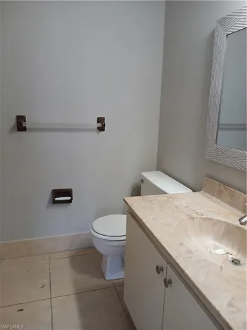 Bathroom featuring a stone-top vanity with an integrated sink, neutral floor tile, wall-mounted towel bar, and a framed mirror. Primary bathroom