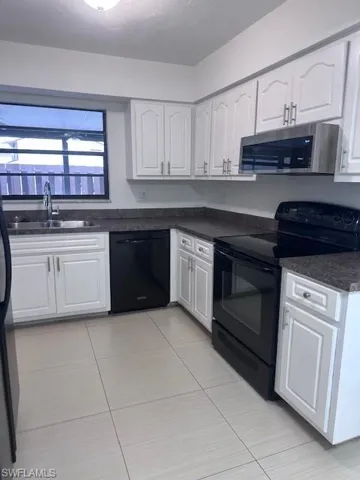 Kitchen featuring white cabinetry, dark stone-finish countertops, stainless steel microwave, black range, and light-toned ceramic tile flooring