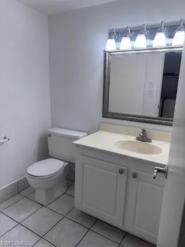 Bathroom featuring a vanity with neutral stone-finish countertop, undermount sink, framed wall mirror, multi-bulb vanity lighting, and ceramic tile flooring. Downstairs half bathroom