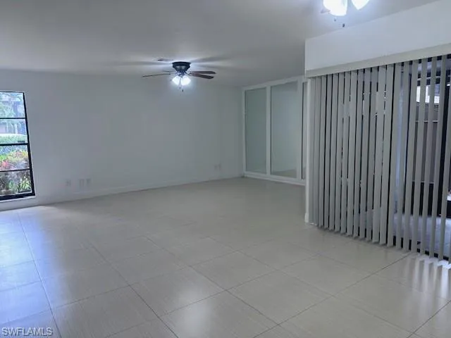 Neutral-toned large-format tile flooring, multi-pane window, ceiling fan with integrated lighting, and full-height sliding glass doors featuring vertical blinds