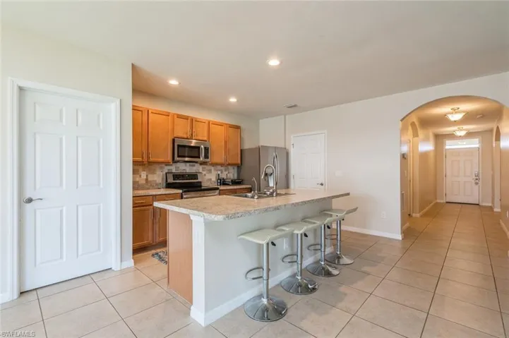 Kitchen featuring stainless steel appliances, tasteful backsplash, a kitchen island with sink, sink, and light tile floors