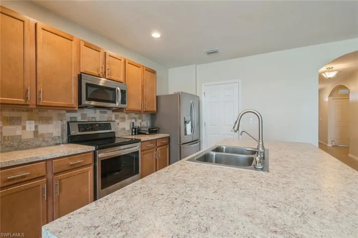 Kitchen with sink, light stone counters, tasteful backsplash, and appliances with stainless steel finishes