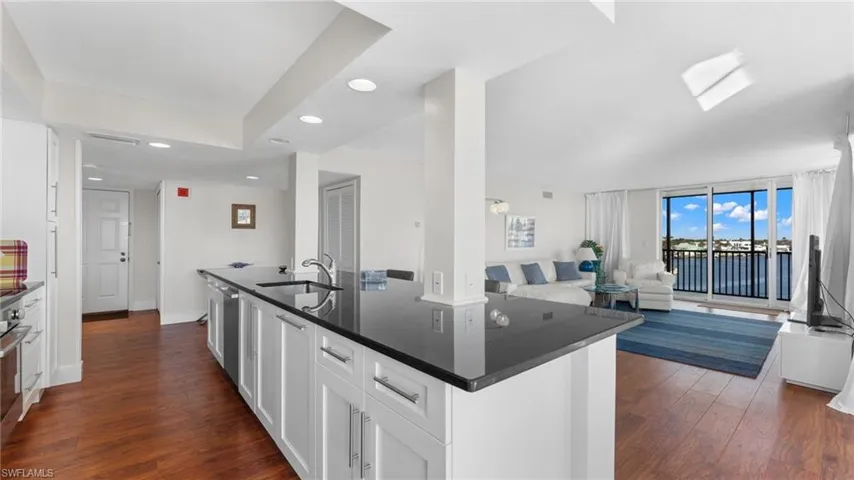 Kitchen featuring stainless steel dishwasher, dark stone counters, dark wood-type flooring, sink, and white cabinetry