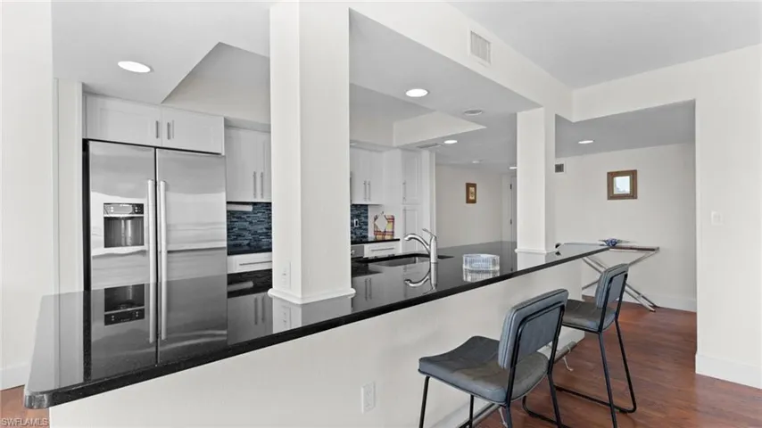 Kitchen with white cabinetry, kitchen peninsula, stainless steel fridge with ice dispenser, and decorative backsplash