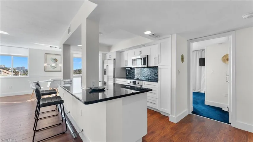 Kitchen featuring backsplash, dark hardwood / wood-style floors, appliances with stainless steel finishes, white cabinetry, and a breakfast bar area