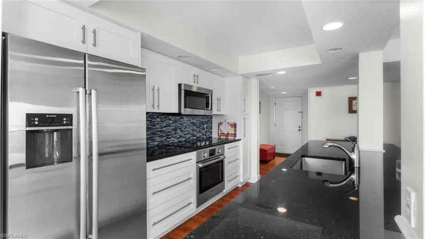 Kitchen featuring dark wood-type flooring, dark stone counters, white cabinets, sink, and appliances with stainless steel finishes
