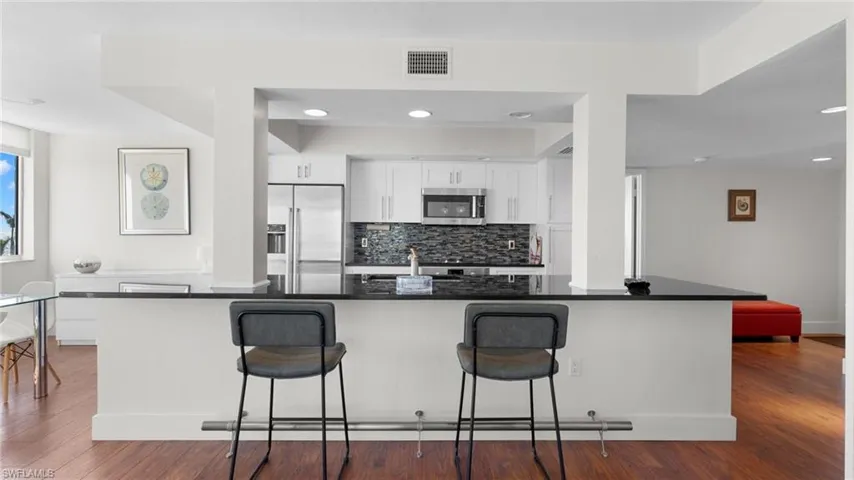 Kitchen featuring white cabinets, dark hardwood / wood-style floors, stainless steel appliances, and a breakfast bar area