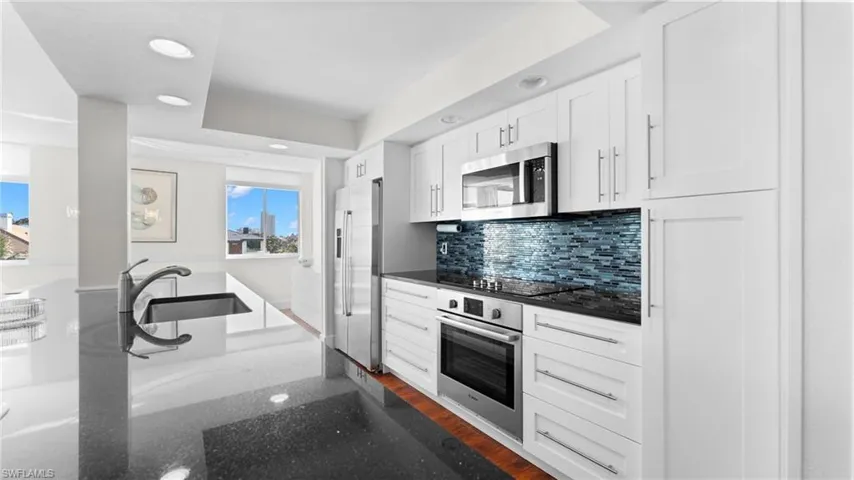 Kitchen with white cabinetry, stainless steel appliances, dark hardwood / wood-style flooring, backsplash, and dark stone counters