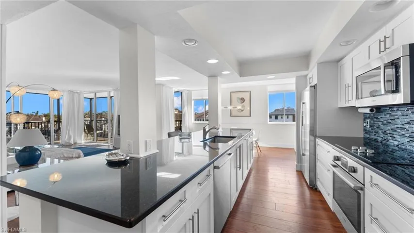 Kitchen with appliances with stainless steel finishes, dark hardwood / wood-style flooring, tasteful backsplash, a center island with sink, and white cabinetry