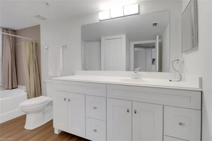 Full bathroom with wood-type flooring, toilet, vanity, and shower / tub combo with curtain